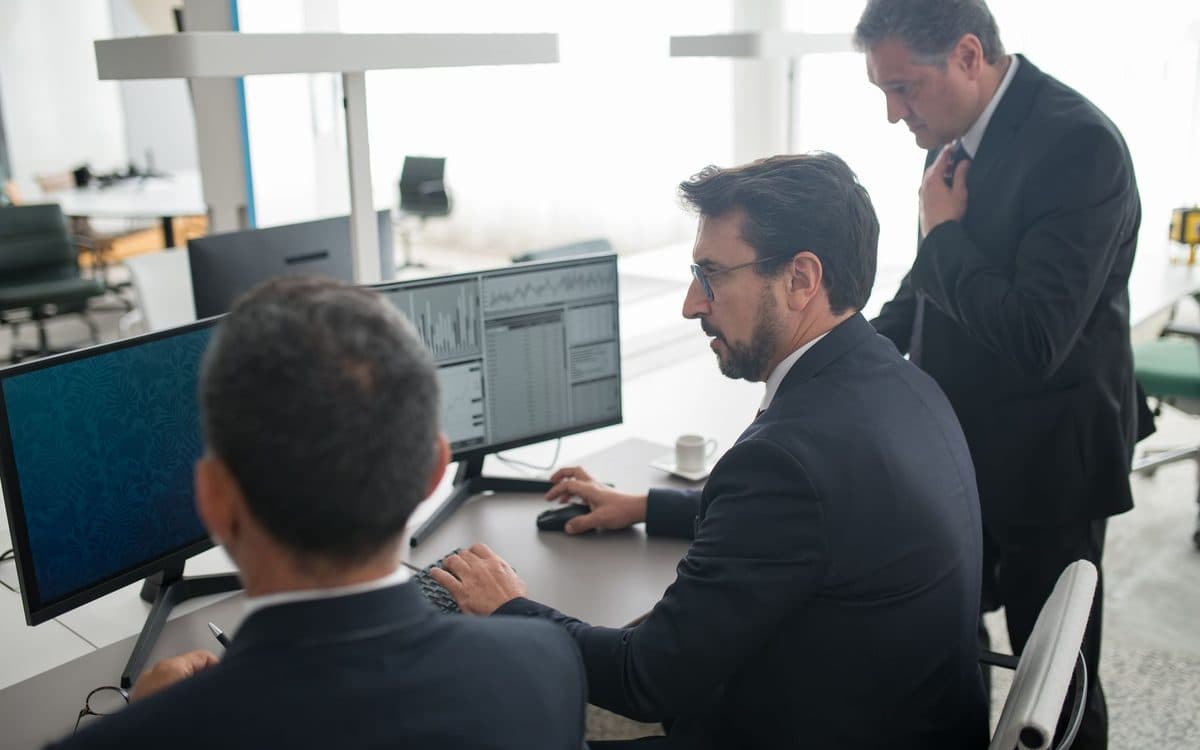 Two analysts working through data tables on a pair of monitors